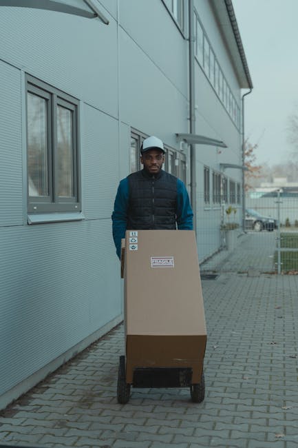 Courier delivering a package on a trolley outside a modern industrial building.